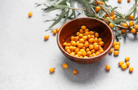 Sea buckthorn berries filling a wooden bowl with branches and scissors on a gray surface
