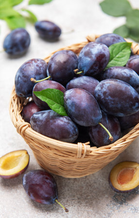 Plums filling a wicker basket with leaves, showing ripe fruit and slicesの写真素材