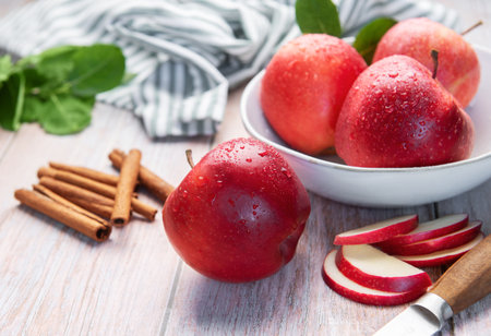 Red apples, cinnamon sticks, and sliced apples on a wooden surface, ready for cookingの写真素材