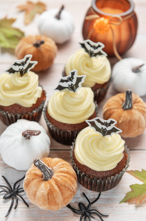 Festive halloween cupcakes, decorative pumpkins, and spiders adorning a light wooden surfaceの写真素材