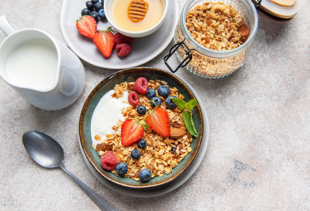 Granola bowl with yogurt, strawberries, blueberries, raspberries, mint, and almonds on a grey...