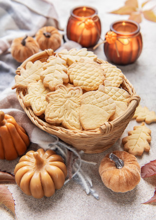 Leaf and acorn shaped autumn cookies in a basket, surrounded by fall decorations and candles