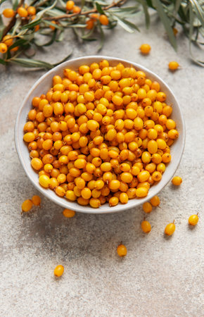 Ripe organic sea buckthorn berries filling a bowl on a textured background with branchesの写真素材