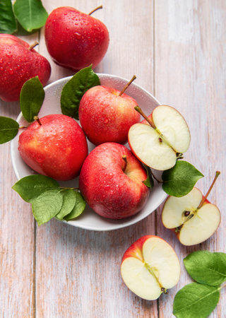 Vibrant red apples, whole and sliced, with green leaves and a knife on a light wooden surface