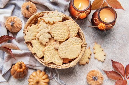 Leaf and acorn shaped autumn cookies in a basket, surrounded by fall decorations and candlesの写真素材