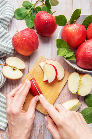 Hands slicing a red apple on a wooden cutting board with more fresh apples aroundの写真素材
