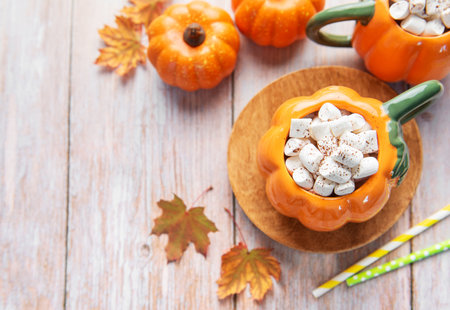 Pumpkin shaped mugs filled with hot chocolate and marshmallows, celebrating fall seasonの写真素材