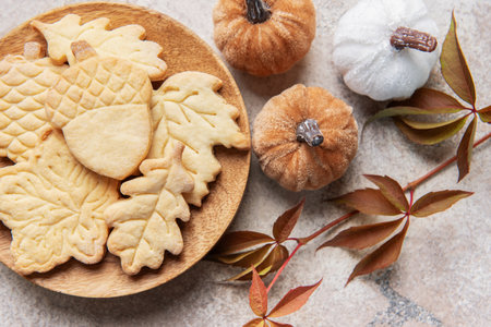 Sweet butter cookies shaped as fall leaves and acorns on a wooden plate, surrounded by decorative pumpkins and autumn foliageの写真素材