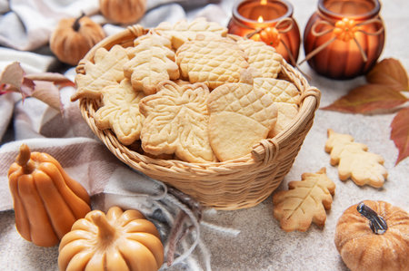 Leaf and acorn shaped autumn cookies in a basket, surrounded by fall decorations and candlesの写真素材