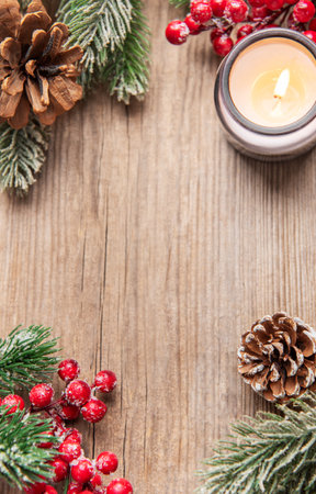 Illuminating candle with pine cones, berries, and frosted fir branches on wooden surfaceの写真素材