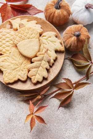 Sweet butter cookies shaped as fall leaves and acorns on a wooden plate, surrounded by decorative pumpkins and autumn foliageの写真素材