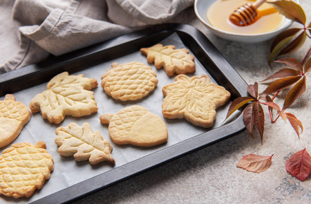 Freshly baked autumn themed cookies arranged on a baking sheet with honey and fall leavesの写真素材