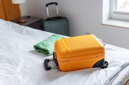 Yellow suitcase and green clothing on a neatly made bed in a hotel roomの写真素材