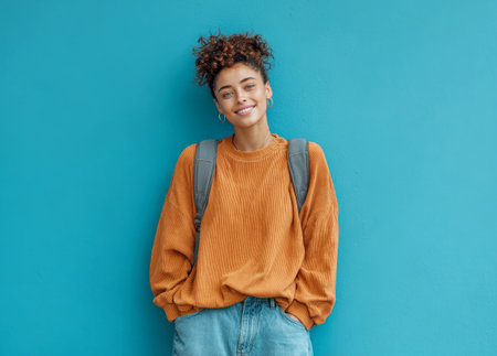 Smiling woman with backpack standing against a blue wall, looking confidentの素材