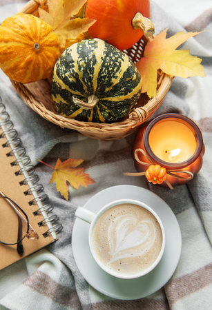 Cozy autumn setting with warm candle light, a cup of coffee, pumpkins, and a notebookの写真素材