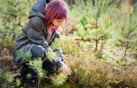 Child with pink hair crouching, discovering a mushroom in a forestの写真素材