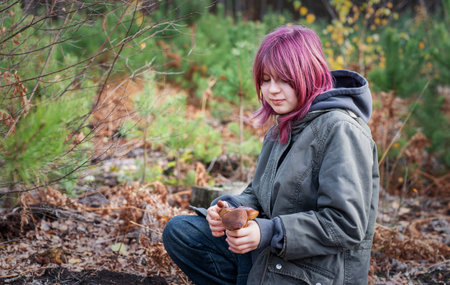Young girl with pink hair holding a mushroom, foraging in an autumn forestの写真素材