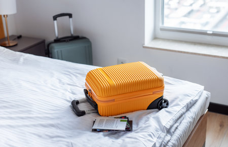 Orange suitcase sitting on a hotel room bed with another luggage and windowの写真素材