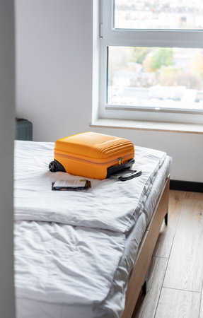 Orange luggage suitcase sitting neatly on a hotel bed, ready for travel or departureの写真素材