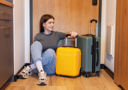 Woman sitting on floor with two suitcases, patiently waiting for arrival or departureの写真素材