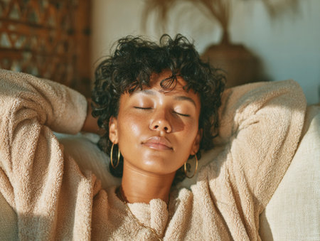 Young woman with closed eyes resting on a couch, feeling calm and sereneの素材