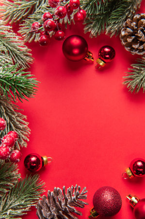 Festive christmas border with frosted fir branches, red berries, and ornaments on a red backgroundの写真素材