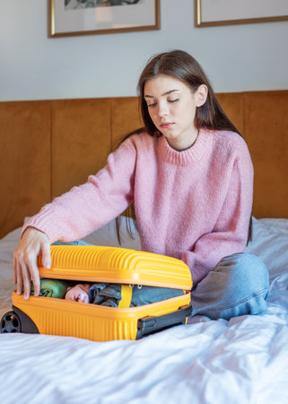 Woman preparing luggage on a bedroom bed, getting ready for a journeyの写真素材