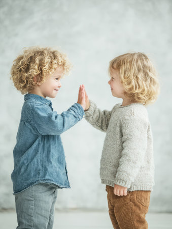 Two smiling children with curly hair high fiving, representing connection and childhood joyの素材