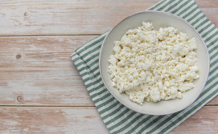 Cottage cheese in a white bowl, sitting on a striped napkin over a rustic wooden surface