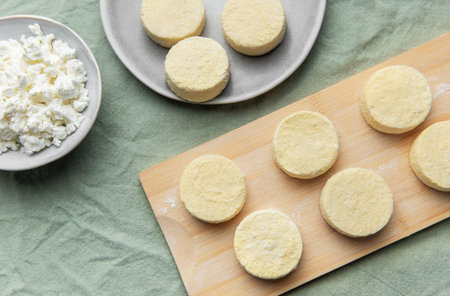 Flat lay of raw syrniki pancakes and cottage cheese on a table ready for cookingの写真素材