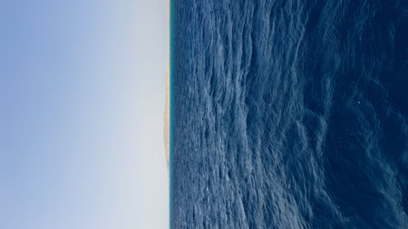 Expansive ocean waves undulate under a bright sky, with a sandy island appearing in the distance, evoking a sense of peace and natural beautyの写真素材