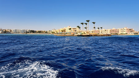 Coastal scene showcases colorful buildings and palm trees by the water, with calm waves and a clear sky enhancing the serene environment. Red Sea. Hurghada. Egyptの写真素材