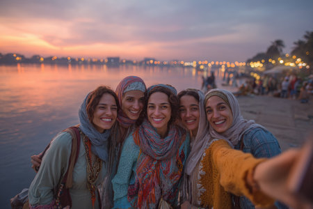Group of Egyptian women enjoying a moment by the Nile river, capturing selfies against a stunning sunset backdrop, highlighting their joyful expressions and vibrant attireの素材