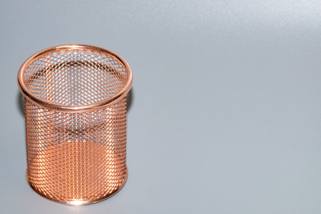 Copper mesh pencil holder placed on a sleek gray surface, highlighting its unique design and texture, perfect for organizing stationery and adding style to any workspaceの写真素材