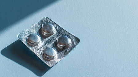 Silver blister pack positioned diagonally on a soft blue background, casting gentle shadows, offering a clean and minimalist look with ample copy space for creative useの素材