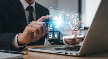 Businessman interacting with a futuristic holographic interface displaying digital icons and data analytics on a laptop screenの素材