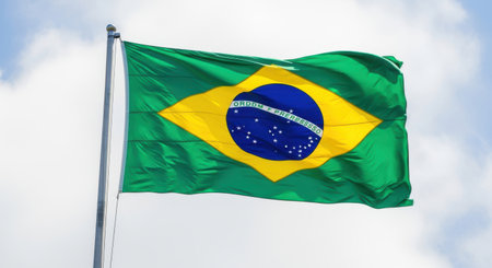 The vibrant green and yellow flag of brazil waving proudly against a bright cloudy skyの素材