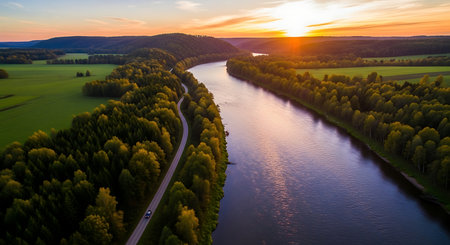 An aerial drone shot captures a tranquil river winding through vibrant green forests as the sun sets, casting a warm glow.の素材