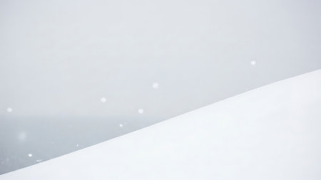 Gentle snowfall blankets a serene winter landscape with soft white drifts and a muted gray backgroundの素材