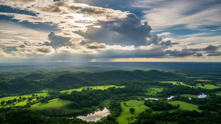 An aerial view of vibrant green hills, a reflective body of water, and a dramatic sky with sunlight piercing through clouds.の素材