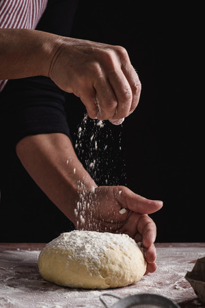 woman preparing dough with her hands on a dark backgroundの写真素材