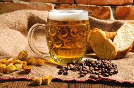 A glass of fresh cold light beer with bread and wheat on burlapの写真素材