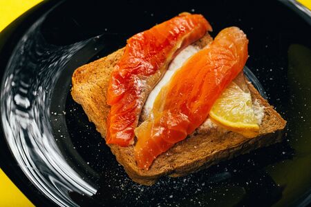 tasty healthy toast with butter, salmon and lemon on a black glossy plate on a yellow background. close top view, macroの写真素材