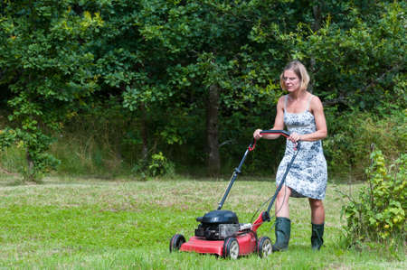 Young blond woman cutting grass with a lawn mower の写真素材