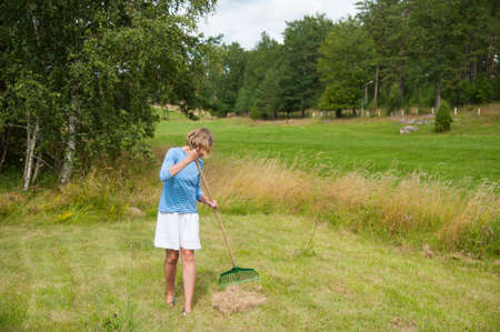 Young woman is raking hay on a meadow in the swedish countrysideの写真素材