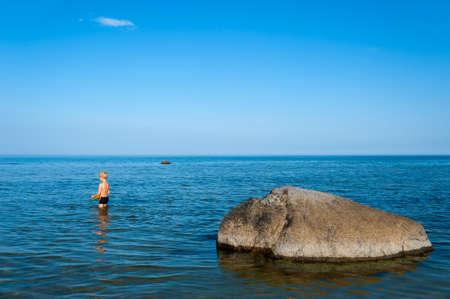 Young boy standing in the water near the beach close to a rock and enjoying the warm summer weather, island Oeland, Sweden の写真素材