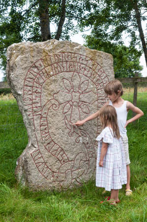 Two children study the  rune stone of Bjärby after a bath in the Baltic Sea nearbyの写真素材