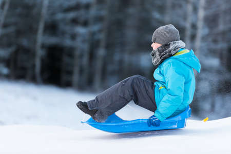 Young boy sledging downhill om a blue sledge on a winter dayの写真素材