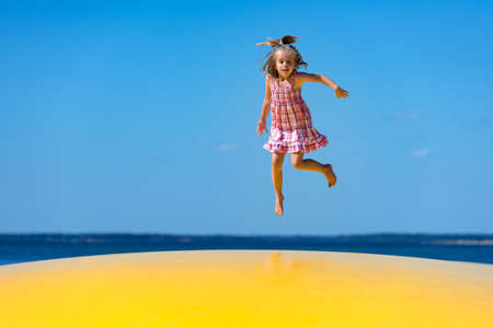 Cute little girl with pigtail jumping on to inflatable trampoline at the beach.の写真素材