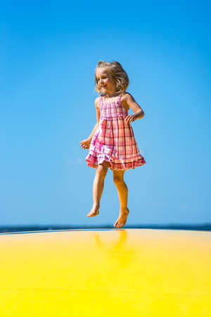 Cute little girl with pigtail jumping on to inflatable trampoline at the beach.の写真素材
